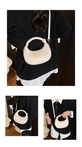 Detail of a minimalist off-white semi-circular handbag with a unique curved tube handle