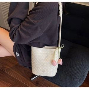 Detail of woven leather bucket bag with pink tulip charms and braided shoulder strap