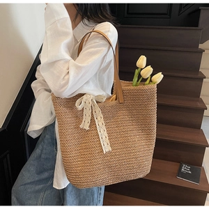 Detail of woven straw tote bag with brown leather handles and a white lace bow accent