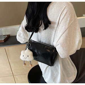 Details einer glänzenden schwarzen Zylindertasche mit Silberreißverschluss und Anhänger