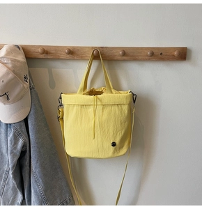 Detail of yellow nylon drawstring bucket bag hanging with denim jacket and beige cap