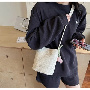 Close-up of white woven bucket bag with pink tulip charm and braided handle