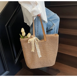 Detailed close-up of a large beige woven straw tote bag with a white lace bow detail