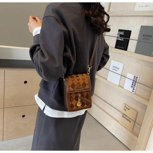 Close-up of brown quilted phone bag with vintage pattern and gold metal charm