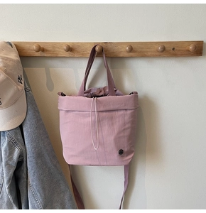 Pink nylon drawstring tote bag hanging on wooden hook with casual fashion accessories