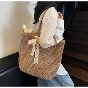 Detail of woven straw tote bag with brown leather straps and a white lace bow accent