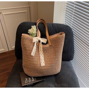 Detail of hand-woven straw tote bag featuring cream lace bow and premium leather handles