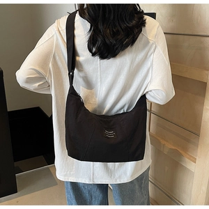 Close-up of black canvas crescent bag with wide shoulder strap and woven label