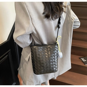 Close-up of black woven bucket bag with blue tulip charm on a grey blazer outfit
