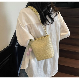 Detail of a woven bucket bag in pale yellow leather with purple floral charms and wide strap