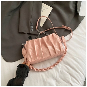 Détail du sac nuage plissé rose avec poignée tressée et chaîne argentée sur le lit