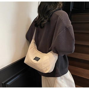 Detail of a beige crescent nylon crossbody bag worn by a model in a minimalist setting