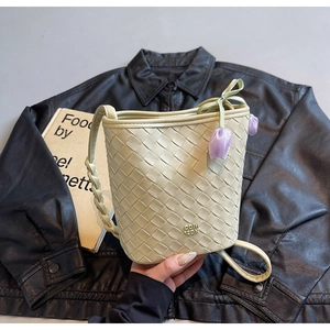 Detail of hand-woven cream bucket bag featuring a gold logo and purple tulip charm