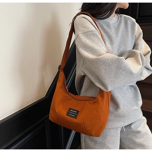 Detail of orange crescent tote bag with black slogan patch worn with casual gray hoodie