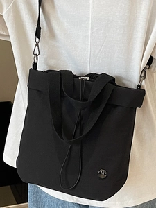 Fashionable black canvas drawstring tote bag with crossbody strap and metallic M logo