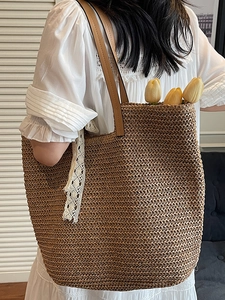 Brown woven straw tote bag with lace ribbon and leather handles shown on a model