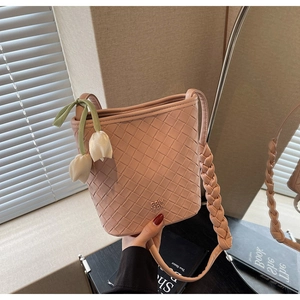 Detail of woven pink bucket bag featuring a tulip charm and braided shoulder strap
