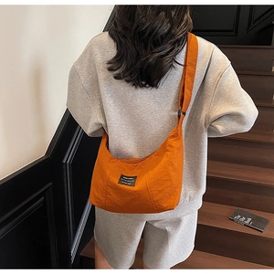 Detail of a bright orange crescent crossbody bag with brand label on nylon material