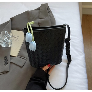 Detail of black woven bucket bag with blue tulip charm and knotted strap on blazer