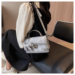 Detail of greyish-white floral crossbody bag with silver twist lock and puppy charm