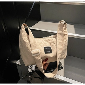 Detail view of cream nylon tote bag featuring adjustable strap and black logo patch