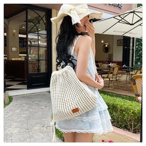 Detail of cream crochet drawstring backpack with woven net pattern and leather logo patch