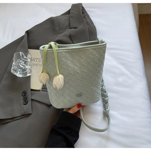 Detail of light green woven bucket bag featuring elegant white tulip leather tassels