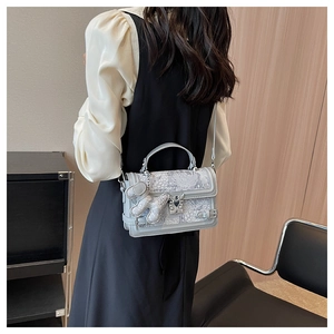 Detail of light grey shoulder bag with white floral embroidery and cute dog charm pendant