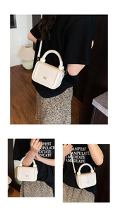 Detail of creamy white litchi grain leather bag with unique arched handle and metallic logo