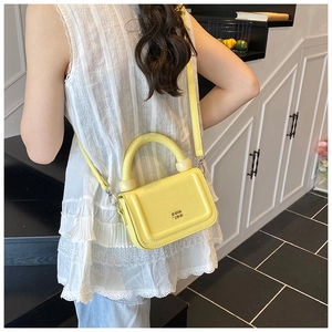 Detail of a bright yellow leather crossbody bag featuring a curved top handle and chain strap