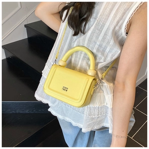 Detail of a bright yellow lychee leather handbag with a gold logo on wooden stairs