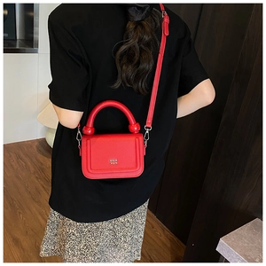 Detail of red textured leather bag with bold curved handle and metallic logo plaque