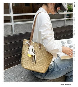 Detail of hand-woven straw tote bag with brown leather straps and cute chick charm accessory
