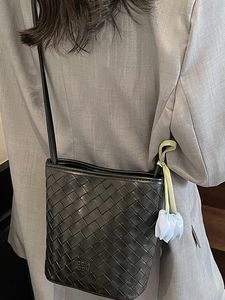 Minimalist black woven leather bucket bag with a blue tulip charm on a grey blazer back
