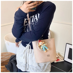 Detail van de geweven crème bucket bag met parelketting en cartoon hanger sieraad