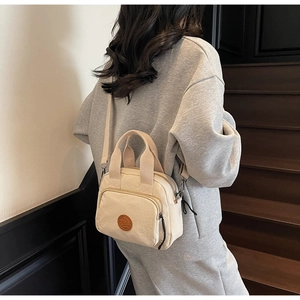 Close-up of cream canvas mini square bag with brown leather logo and front zipper pocket