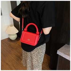 Close-up of red pebbled leather shoulder bag with bold handle and COIN QON logo details