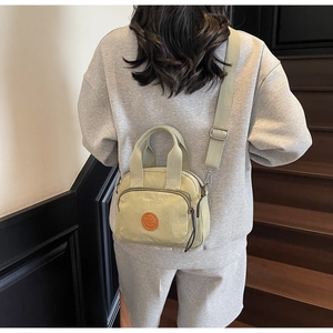 Model wearing a light green nylon crossbody bag with dual zippers and adjustable strap