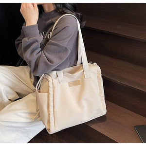 Detail of a beige canvas tote bag showing side storage pocket and leather brand logo