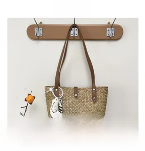 Detail shot of woven straw tote bag with brown leather handles and small chick pendant