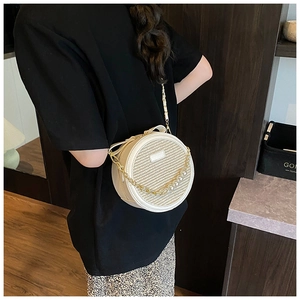 Détail d'un sac bandoulière rond beige avec sangle en perles et chaîne dorée élégante