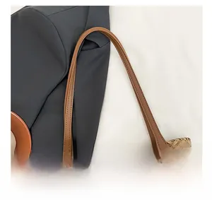 Detail shot of straw tote bag showing brown leather handle with silver rivets on woven texture