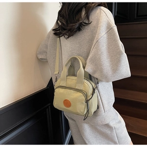 Detailed view of light green nylon crossbody bag with brown leather logo patch on a model
