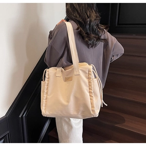 Detailed side view of beige canvas tote bag with drawstring texture and long shoulder straps