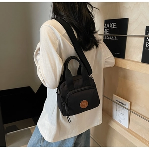 Detail of a black nylon crossbody bag with leather logo and adjustable wide strap