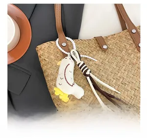 Detail of cute white plush bird charm with tassel on a straw woven tote bag handle