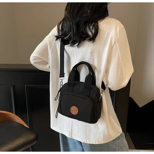 Macro shot of stylish black nylon crossbody bag featuring a classic brown leather logo patch