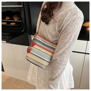 Détail d'un sac seau en paille tissée colorée avec charms fraises et bandoulière en cuir