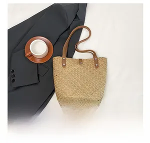 Flat lay of straw tote bag with brown leather handles and silver rivet details
