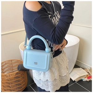 Detail of light blue lychee pattern leather bag with thick round handle and metal logo